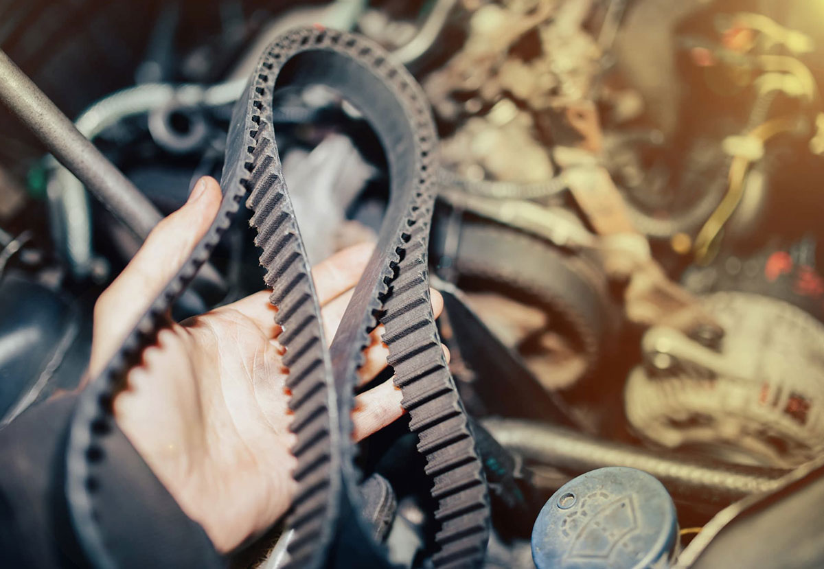 Hand holding a vehicle belt with a blurred car engine as background