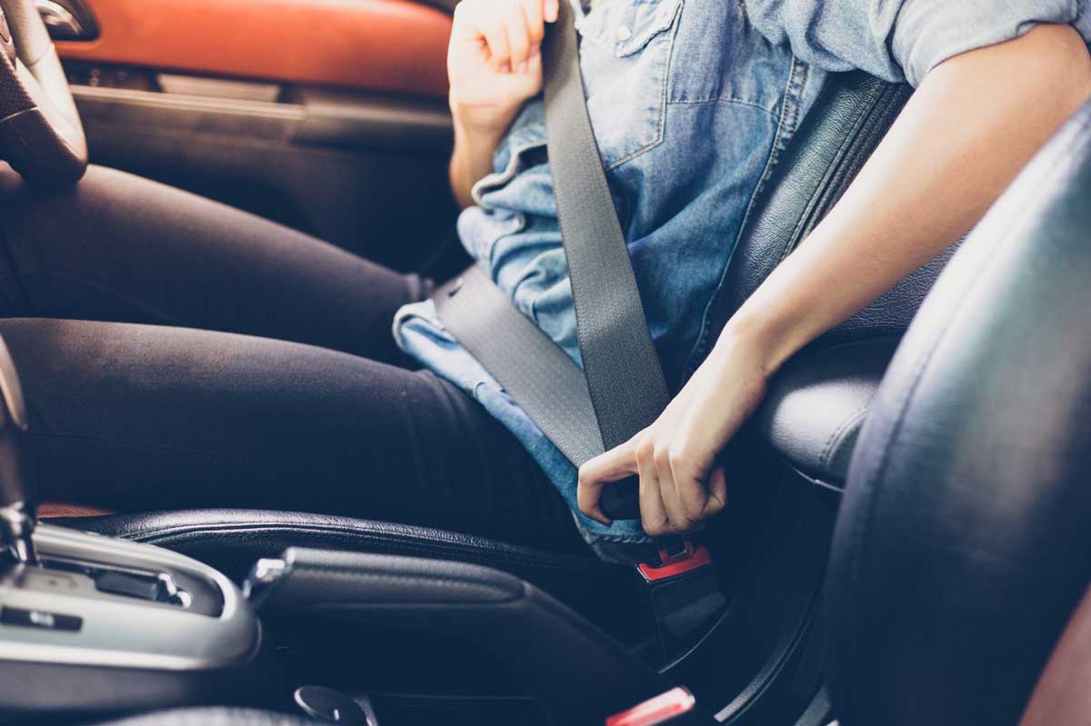 A photo with a person sitting on a car getting the seat belt on