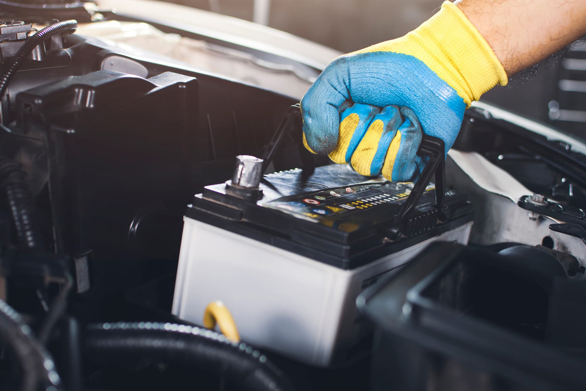 Hand holding a car battery to take it out of the car for maintenance