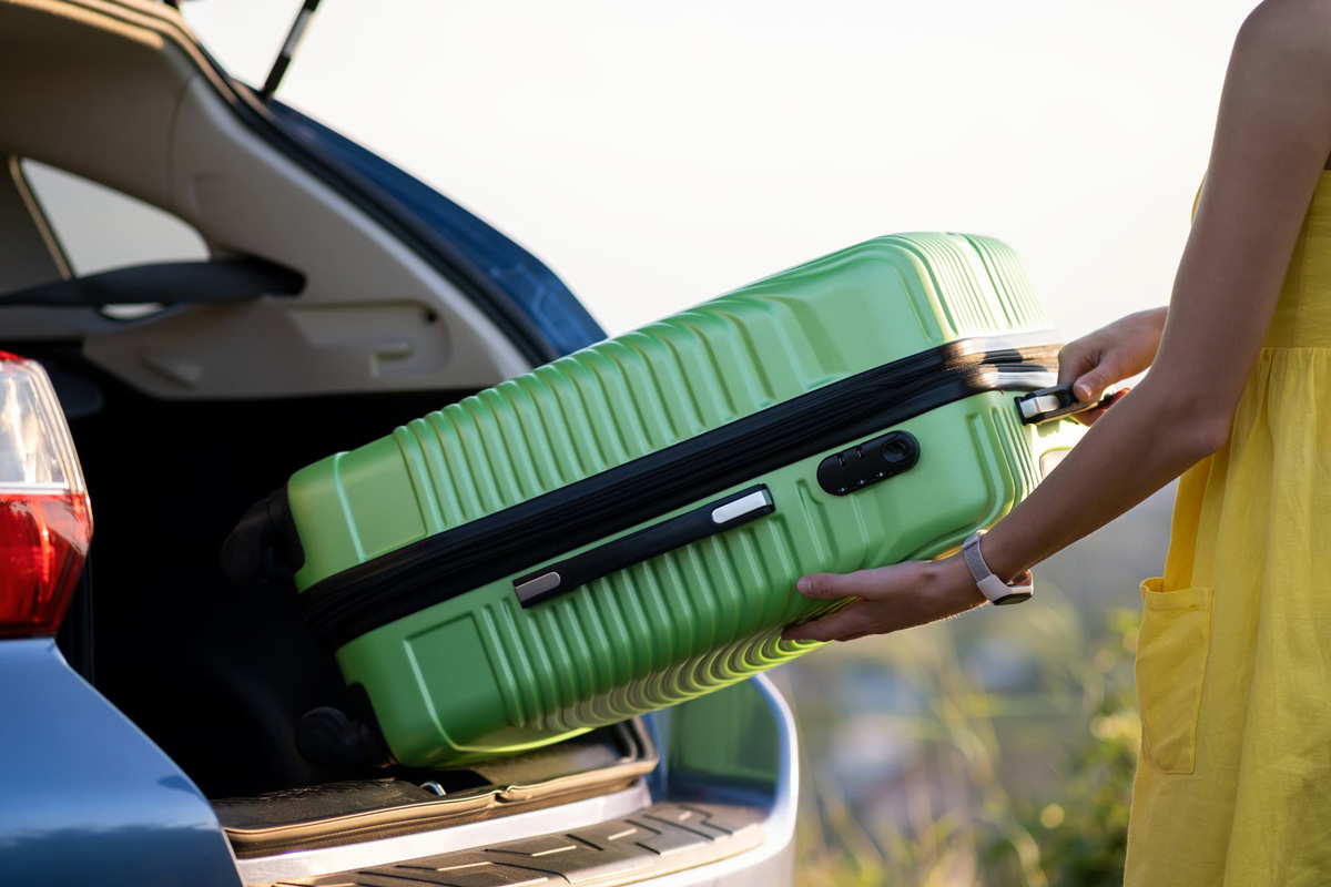 Woman in a yellow dress taking a green suitcase out of a vehicle