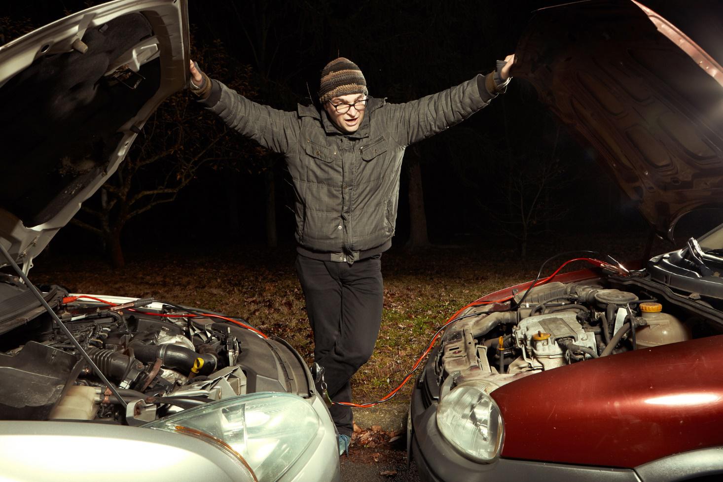 Driver jump starting dead car battery with another car